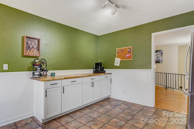 bar featuring a wainscoted wall, rail lighting, freestanding refrigerator, and a textured wall