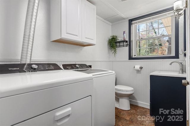 clothes washing area with a sink, separate washer and dryer, wainscoting, and laundry area