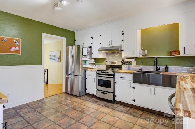 kitchen with under cabinet range hood, appliances with stainless steel finishes, white cabinetry, and wooden counters