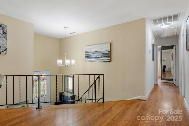 hall featuring visible vents, an upstairs landing, a notable chandelier, wood finished floors, and attic access