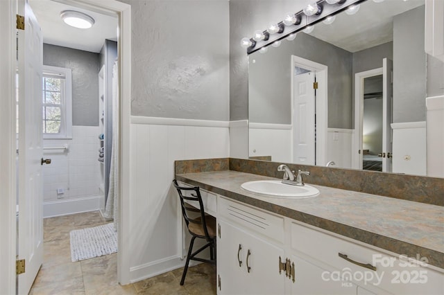 full bath featuring a wainscoted wall, a shower with curtain, vanity, and a textured wall