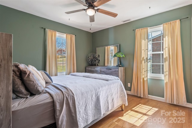 bedroom with light wood finished floors, visible vents, a ceiling fan, and baseboards