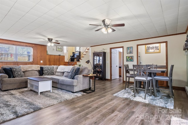 living area with ornamental molding, wood finished floors, stairway, baseboards, and ceiling fan