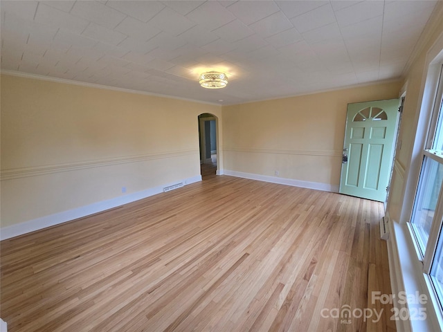 unfurnished room with visible vents, crown molding, baseboards, light wood-style floors, and arched walkways