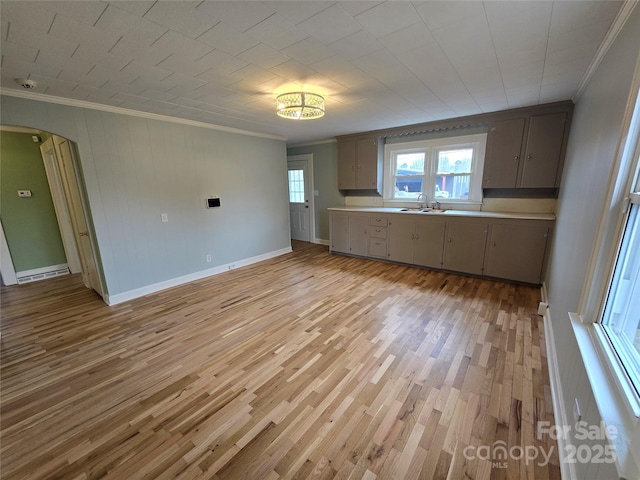 kitchen with light countertops, light wood-style flooring, arched walkways, and ornamental molding