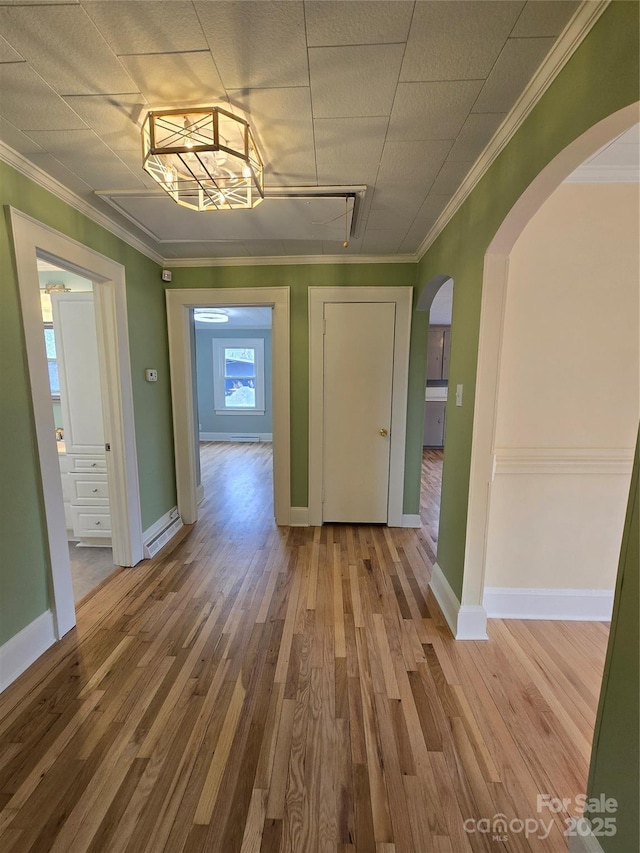 corridor with crown molding, wood finished floors, and arched walkways