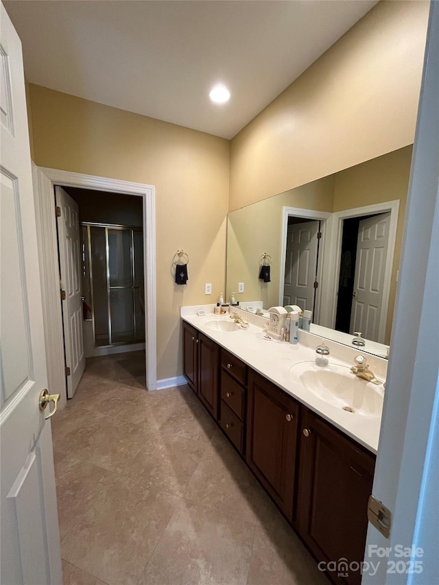 bathroom with double vanity, a stall shower, baseboards, and a sink