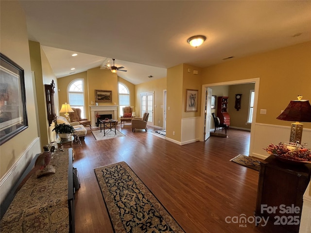 living room featuring dark wood-style floors, visible vents, a fireplace, ceiling fan, and vaulted ceiling