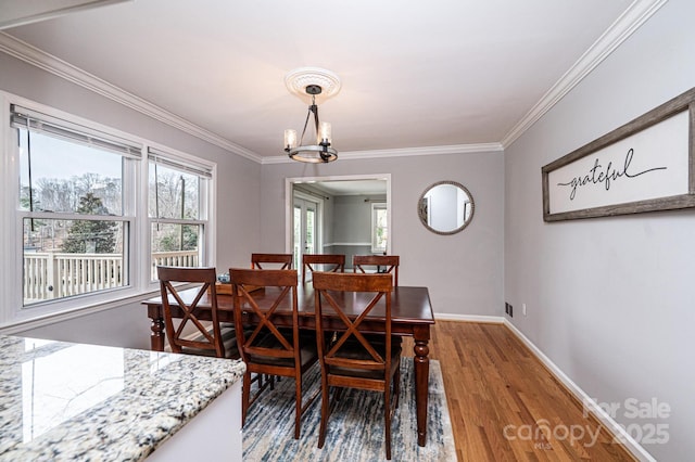 dining space featuring baseboards, a notable chandelier, wood finished floors, and crown molding