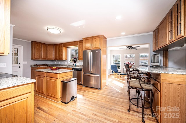 kitchen with a sink, light stone counters, light wood-style floors, and appliances with stainless steel finishes