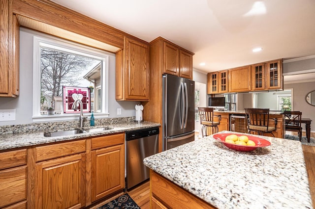 kitchen featuring brown cabinetry, light stone countertops, stainless steel appliances, and a sink