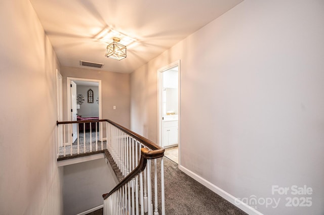 hall with carpet, an upstairs landing, visible vents, and baseboards