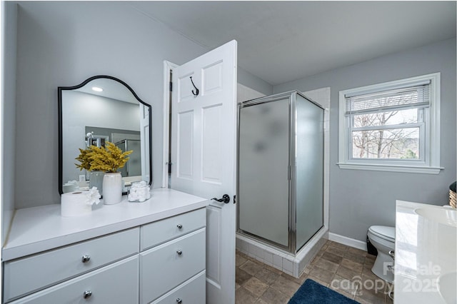 bathroom featuring vanity, baseboards, a shower stall, stone finish floor, and toilet