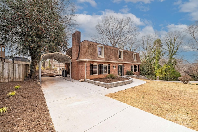 view of front of property featuring driveway, mansard roof, fence, a detached carport, and brick siding