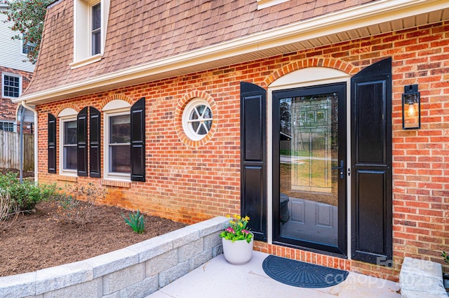 property entrance featuring brick siding and a shingled roof