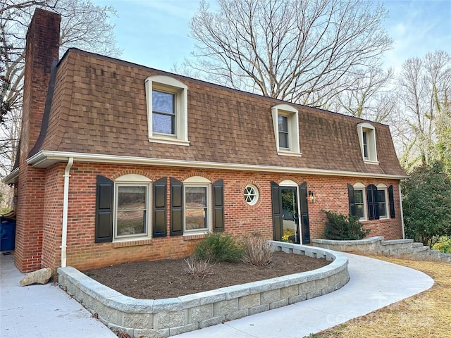 view of front of home with brick siding, mansard roof, and a shingled roof