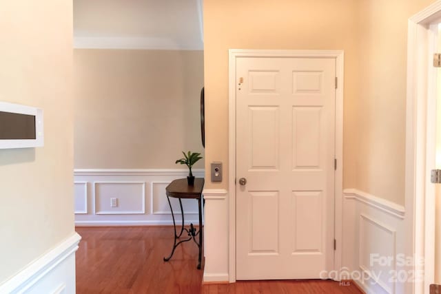 hallway with wood finished floors, wainscoting, and a decorative wall
