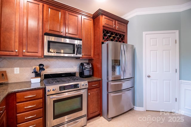 kitchen with dark stone countertops, brown cabinetry, ornamental molding, decorative backsplash, and appliances with stainless steel finishes