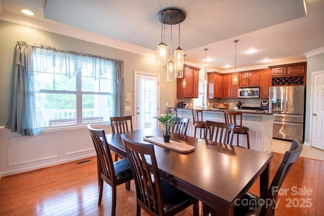dining room featuring a wainscoted wall, visible vents, light wood-style flooring, crown molding, and a decorative wall