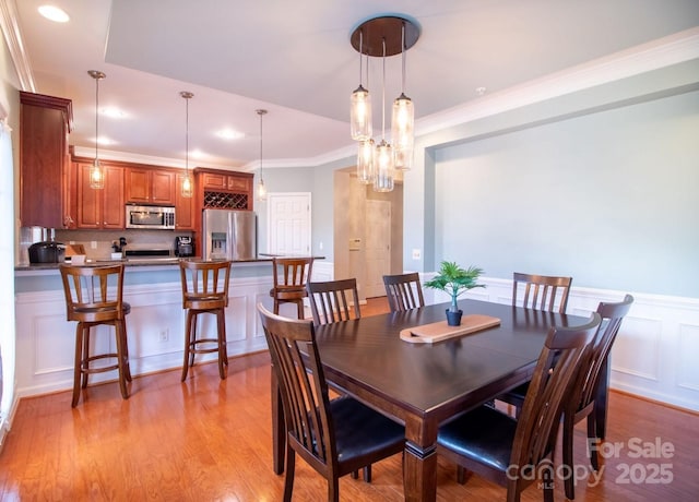 dining area featuring wainscoting, a decorative wall, light wood-style flooring, and crown molding