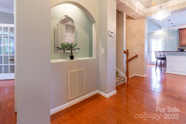 hall featuring visible vents, baseboards, ornamental molding, an inviting chandelier, and wood finished floors