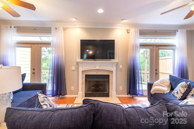 living area featuring french doors, a fireplace with flush hearth, ornamental molding, and a ceiling fan