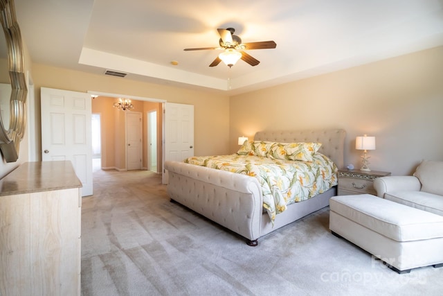 bedroom featuring light carpet, visible vents, ceiling fan with notable chandelier, and a tray ceiling