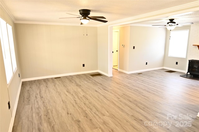 unfurnished living room featuring wood finished floors, a wood stove, ceiling fan, and ornamental molding