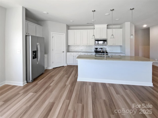 kitchen featuring light wood-style flooring, a sink, appliances with stainless steel finishes, white cabinetry, and backsplash