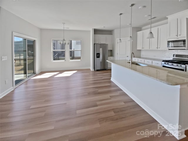 kitchen featuring a sink, light wood-type flooring, white cabinets, stainless steel appliances, and a kitchen island with sink