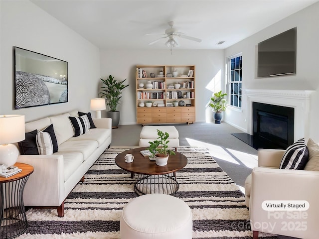 carpeted living area featuring a glass covered fireplace, a ceiling fan, visible vents, and baseboards