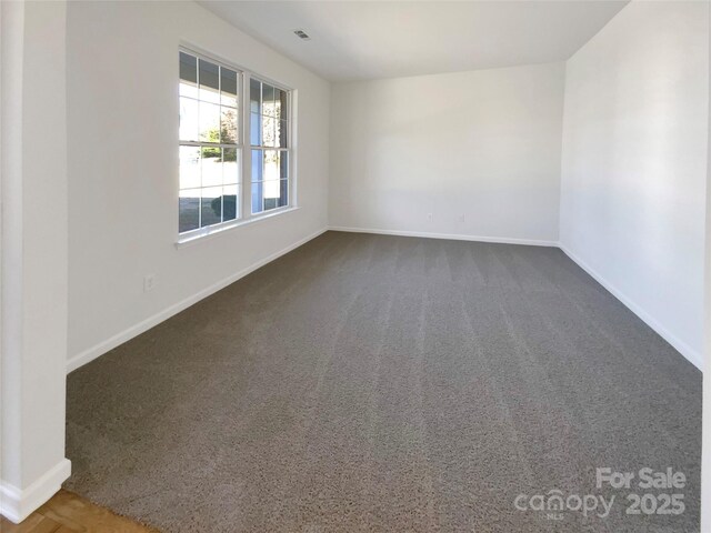 unfurnished room with visible vents, baseboards, and dark carpet