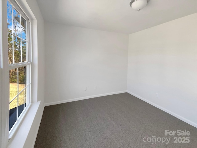 spare room featuring dark colored carpet and baseboards