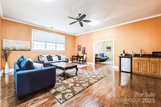 living area with a ceiling fan, baseboards, dark wood finished floors, indoor wet bar, and crown molding