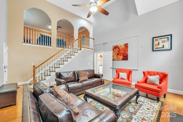 living room with wood finished floors, baseboards, ceiling fan, stairs, and a towering ceiling