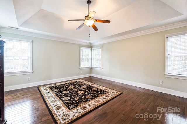 empty room featuring a tray ceiling, baseboards, visible vents, and dark wood-style flooring