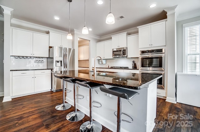 kitchen with crown molding, dark stone counters, a kitchen bar, appliances with stainless steel finishes, and a sink