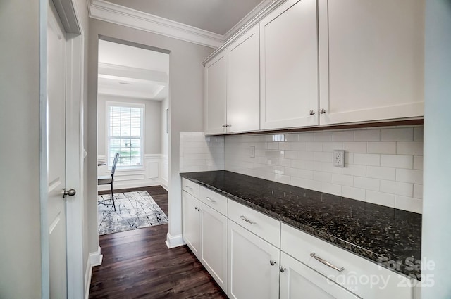 kitchen with dark wood-type flooring, ornamental molding, wainscoting, dark stone countertops, and white cabinets