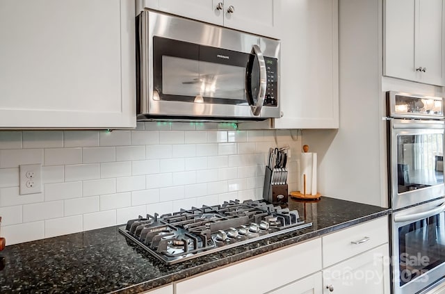 kitchen featuring decorative backsplash, white cabinets, appliances with stainless steel finishes, and dark stone counters