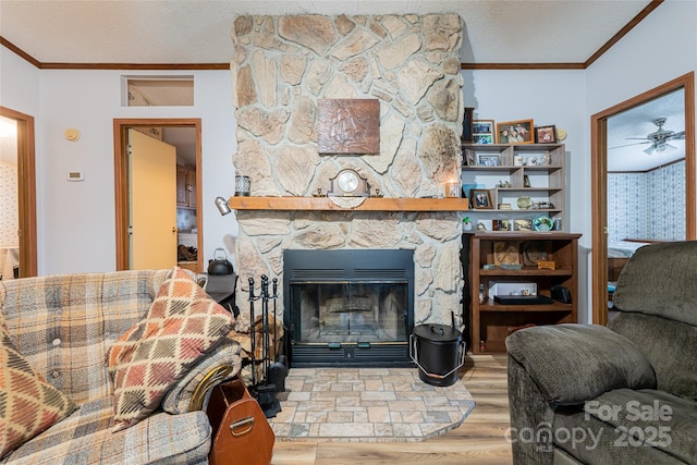 living room with a textured ceiling, a stone fireplace, wood finished floors, and crown molding