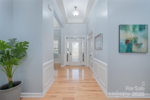 foyer with a decorative wall, light wood-type flooring, a wainscoted wall, and ornamental molding