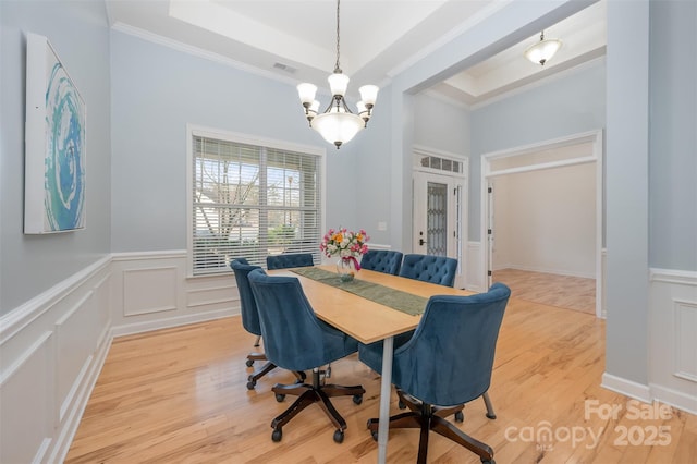 dining space featuring an inviting chandelier, a raised ceiling, light wood-style floors, and visible vents