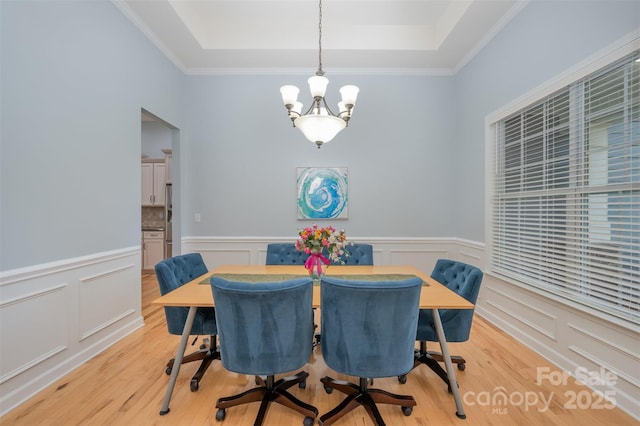 dining room featuring a wainscoted wall, a raised ceiling, light wood-style floors, and a chandelier