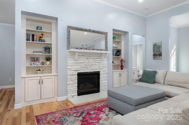 living room featuring built in shelves, baseboards, a stone fireplace, crown molding, and light wood-type flooring