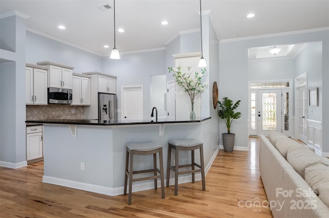 kitchen featuring light wood-type flooring, dark countertops, appliances with stainless steel finishes, and a breakfast bar area