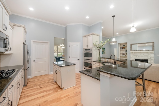 kitchen featuring light wood finished floors, a kitchen island, a breakfast bar area, appliances with stainless steel finishes, and a sink