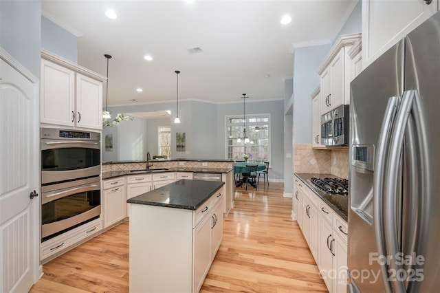 kitchen with light wood finished floors, a peninsula, appliances with stainless steel finishes, crown molding, and backsplash