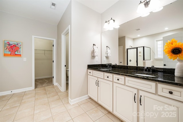 bathroom featuring tile patterned flooring, a shower stall, double vanity, and a sink