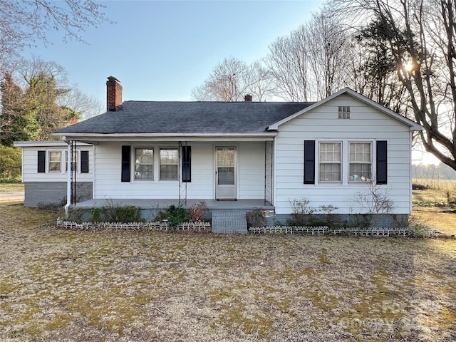 view of front of property featuring a porch, a chimney, and roof with shingles