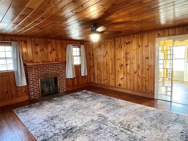 unfurnished living room with a healthy amount of sunlight, a brick fireplace, ceiling fan, and wood-type flooring